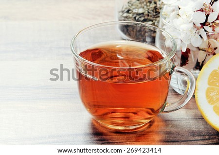 Black tea in a cup on a wooden table. next to a cup of tea, worth a bouquet of flowers of blossoming apricot and half a lemon