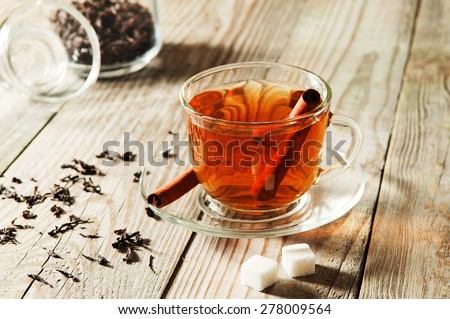 glass cup and saucer black tea with cinnamon standing on a wooden table. Next to a cup of black tea, two pieces are portioned sugar and scattered dry tea