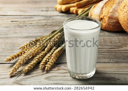 Fresh, homemade milk in a cup made of glass on a wooden table. next to a glass of milk lay wheat ears and  freshly baked bread. rustic style