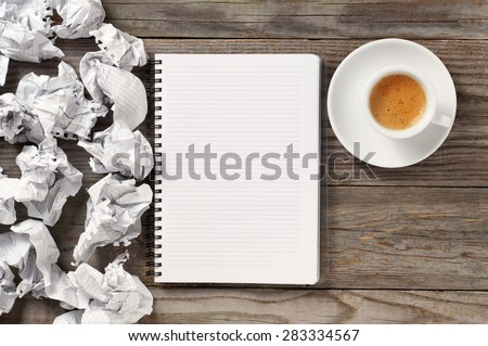 White note pad on a wooden table. Around the notepads lies lot crumpled paper and a cup of black coffee