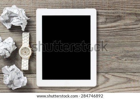 Tablet computer on a wooden table with crumpled paper and white mechanical watch