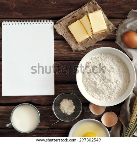 On the old wooden table Open notebook for notes and ingredients for baking - flour, milk, eggs, butter. View from above. Rural background with free text space. Ingredients for the dough