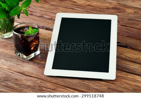 White tablet computer with a glass glass of cola with ice wooden background. The concept, of work outside the office. Top view, Copy space. Free space for text. close up