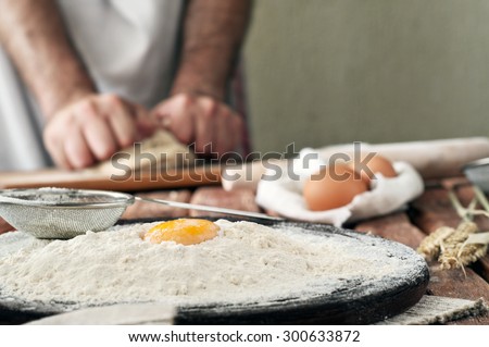 A handful of flour with egg yolk on a wooden table in a bakery. on the background of man hands knead the dough. Rural or rustic. Copy space. Free space for text