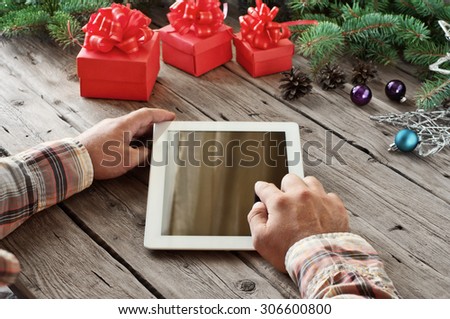 Tablet computer in men hands closeup. Near the table with tablet computer three gift boxes, christmas toys, stars , fir cones and fluffy fir branches. Free space for text. top view. Copy space
