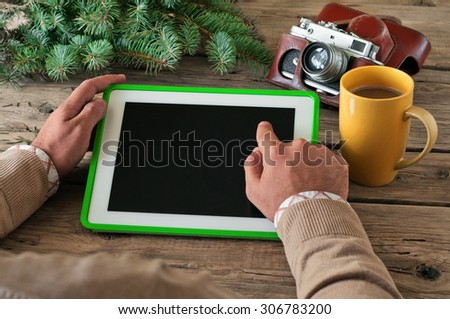 Male hand clicks blank screen tablet computer on the wooden table closeup. Next on the table vintage camera and a large cup of coffee. Copy space. Top view. Free space for text