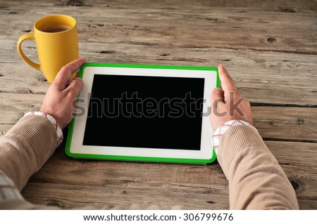 Male hand clicks blank screen tablet computer on the wooden table closeup. Next on the table large cup of coffee. Copy space. Top view. Free space for text