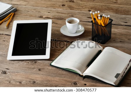 Tablet computer on the wooden desk with an open notepads, pencils and cup of coffee closeup. Free space for text. Top view. Copy space