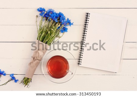 beautiful bouquet of blue wildflowers with an empty memo pad for notes, tea on a white wooden table. Copy space. Free space for text