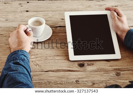 male hands holding a tablet computer with blank screen closeup. Tablet computer with a cup of coffee on the wooden desk. Top view. Copy space. Free space for text. Vintage photo toning