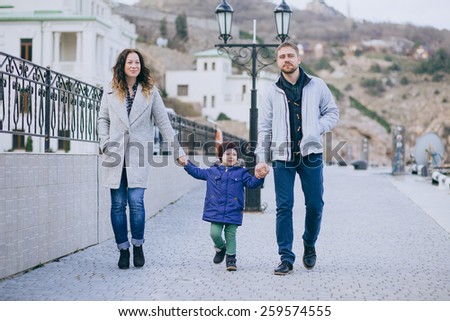 Happy family -mother, father and little son- walking in harbor near sea. Family wearing fashion clothes