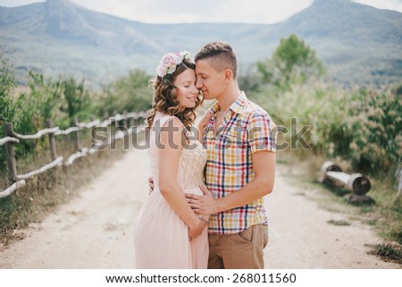Pregnant woman in a pink dress with her husband on the mountains background. Future parents