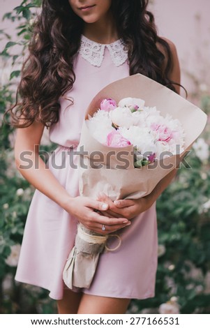 Young beautiful woman with long beautiful hair in a pink dress posing with a bouquet of peonies in a brown paper