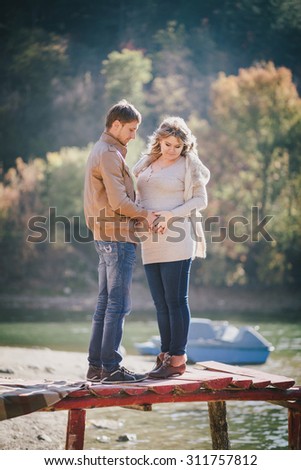Young future parents posing on a wooden bridge and having picnic near lake. Autumn time. Pregnancy