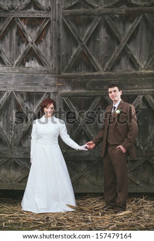 Bride and groom dressed in vintage dress and suit holding hands with wooden door behind them.