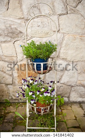 decorative flower bed with pansy in flowerpot, metal white rack with welcome inscription