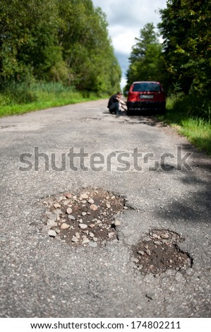 two big holes in old road in forest, man repairing car wheel in shadow