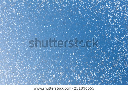 Melting snow spots blue sky background and frozen water texture, condensation on window glass, transparent glass in winter and ice with white snow in contact with morning warm sunlight. Horizontal