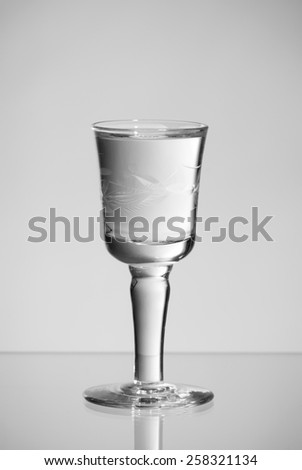 One stem glass of clear vodka alcoholic beverage standing on glass and grey background, vertical orientation, nobody.