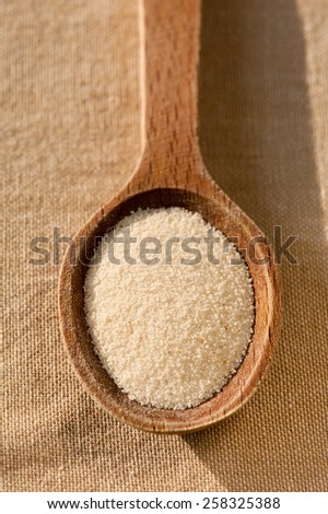 White semolina grains portion on wooden spoon closeup lying on table cloth, coarsely grains healthy raw food heap in day light, vertical orientation, nobody.