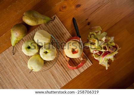 Peeling ripe fruits apples and pears on glass plate on bamboo mat, peelings and whole fruits lying on wooden table, nobody, horizontal orientation, view from above.