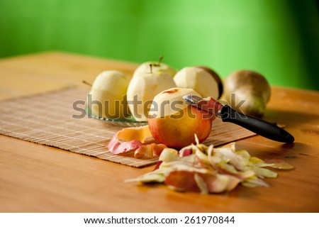 Peeling apples and pears lying on bamboo mat, black peeler, peelings and whole yellow red healthy fruits on wooden table, nobody, horizontal orientation.