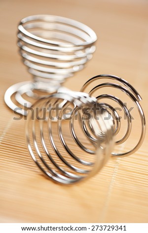 Stainless steel wire egg holder or stand empty utensil on wooden mat in vertical orientation, nobody. Glossy modern kitchen and food accessory.