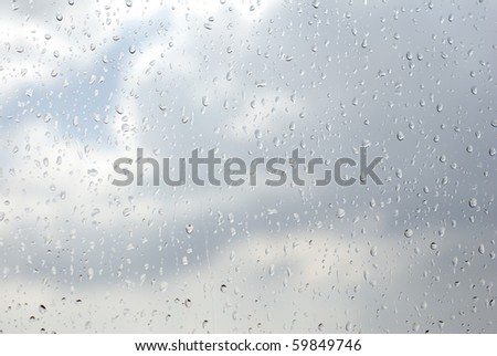 Raindrops flowing down on window glass abstract, cloudy sky visible through transparent glass of window, wet textured background. Horizontal orientation, nobody.