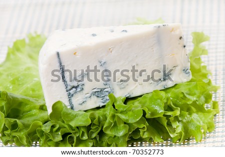 Blue cheese Roquefort portion lying on lettuce green leaf on mat, object in horizontal orientation, nobody, studio shot.