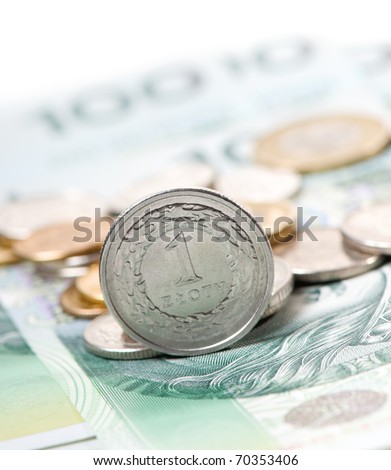 Closeup of one polish zloty coin standing on the edge on green banknote, more coins blurred behind, vertical orientation, nobody.