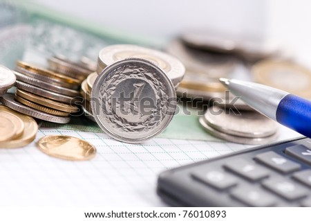 Part of blurred calculator with pen and one value polish zloty coin front view, object standing on the edge on white paper sheet, more coins blurred behind, horizontal orientation, nobody.