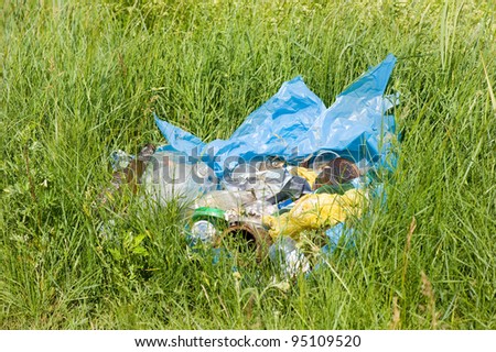 Illegal scatter garbage in blue plastic bag dump in woods lying on fresh grass in early spring season, Clean Up the World gathering in Poland. Earth Day and nature dispose, horizontal orientation
