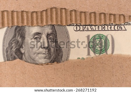 Benjamin Franklin macro peeking through torn corrugated cardboard