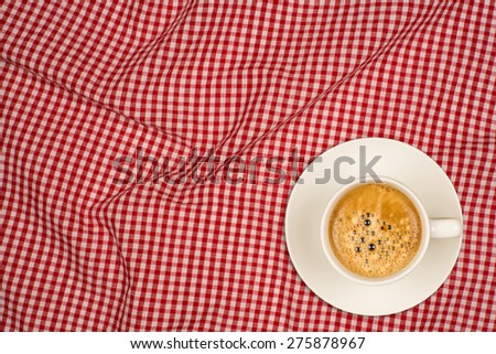 Coffee cup on table. Cup of domestic black coffee ob red and white checkered table cloth background, top view