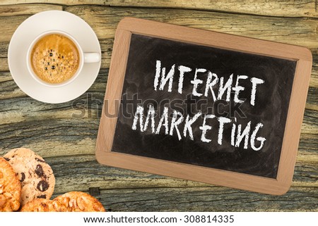 Internet marketing handwritten with white chalk on a blackboard, cup of coffee and biscuit on a wooden background