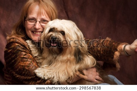 a happy woman with a big smile with her shih-tzu dog in her arm., she is wearing a brown leather jacket