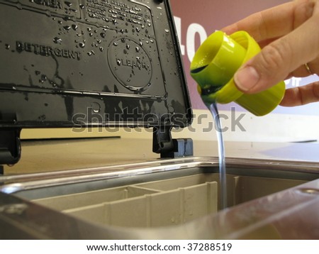 Photo of a woman\'s hand pouring laundry soap into a washing machine