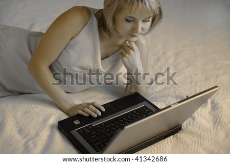 The girl in a works behind the laptop lying on a bed