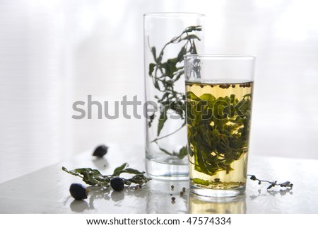 Glass with tea from the leaves and stems of mint on a light background. Around the dry stalks of mint, rose, glass beaker with dried mint.