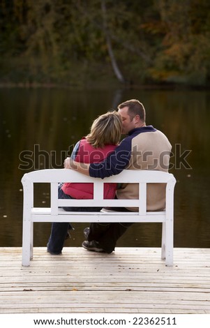 couple kissing on a bench at a lake in autumn