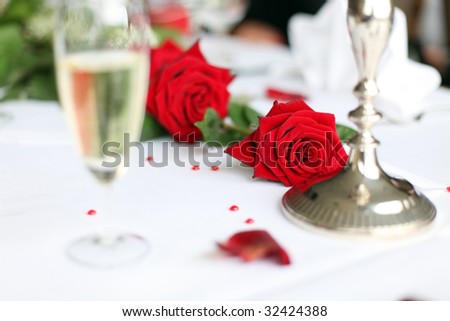 Photo shows a nice red rose on a wedding decorated table with a glass of sparkling wine and some small hearts