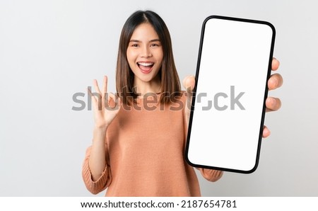 Beautiful Asian woman holding smartphone mockup of blank screen and shows ok sign on grey background Foto d'archivio © 