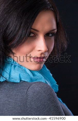 A low key portrait of a gorgeous brunette woman in a grey turtleneck wearing a frilly blue scarf isolated on black background