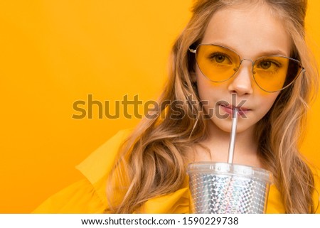 portrait of a blonde in glamorous glasses with a glass for a cocktail on a yellow background