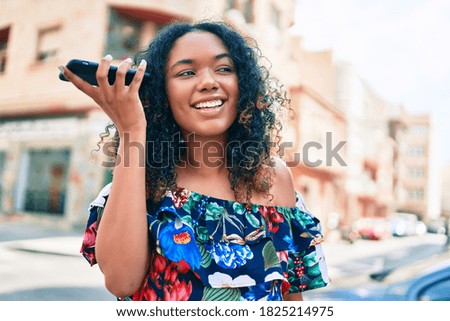 Young african american woman with curly hair smiling happy outdoors listening to voice message on the phone