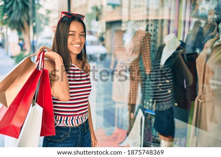 Young latin shopper girl smiling happy holding shopping bags at the city.