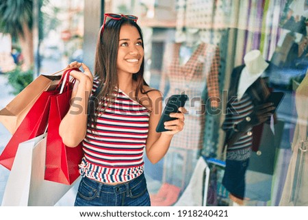 Young latin shopper girl holding shopping bags and using smartphone at the city.
