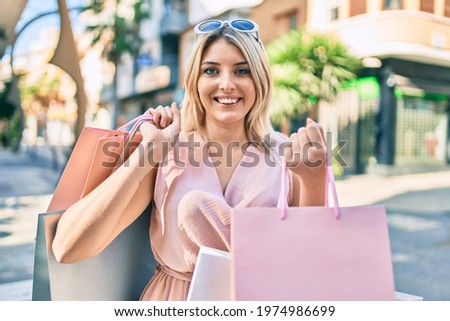 Young blonde woman smiling happy holding shopping bags at the city.