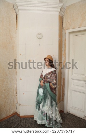 Retro girl in mint dress, Pavlovo Posad shawl, straw hat. Interior, ancient furnace of old traditional national wooden house with carved windows, frames in Moscow city (Russia) on Gastello street, 5