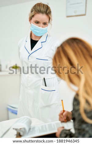 Mass vaccination of the population. Female doctor in a mask gives the patient documents to sign before giving her the Covid-19 antiviral vaccine.